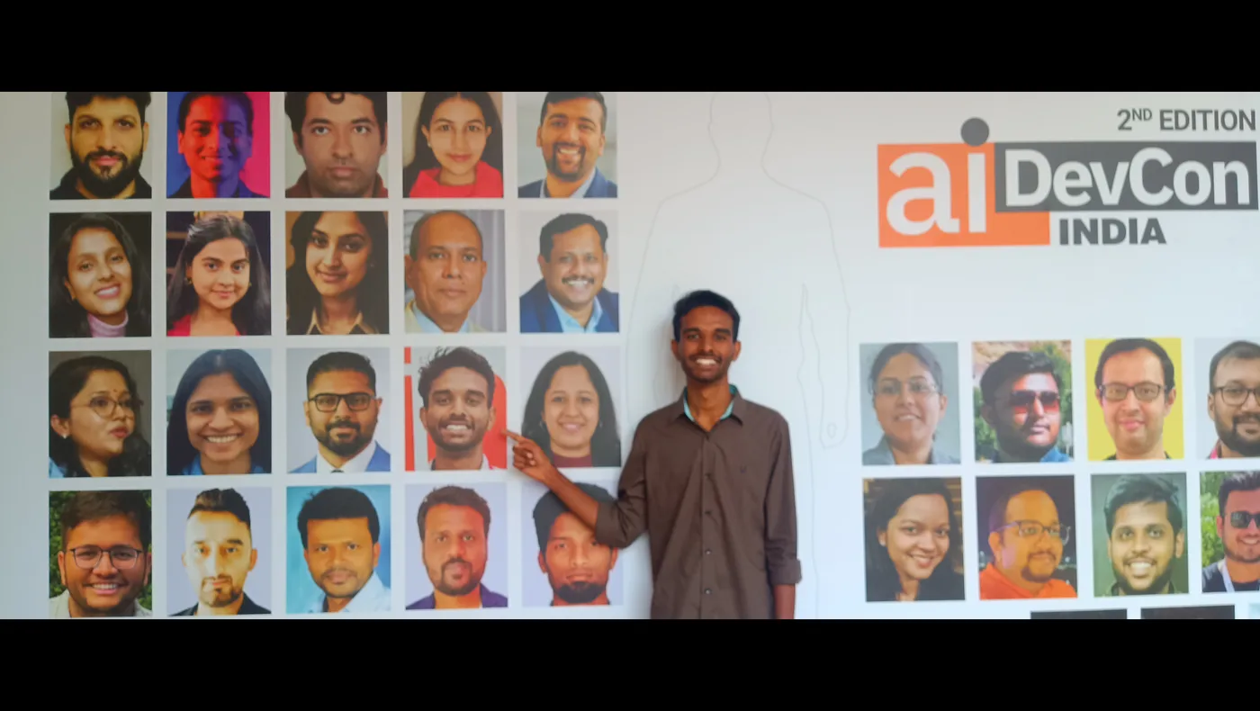 C Sarath Babu pointing at his own photograph on the AIDevCon India 2026 speaker wall