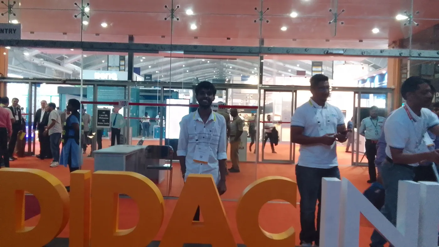 C Sarath Babu's writing on DIDAC INDIA 2023. Standing at the DIDAC INDIA letters at BIEC, Bengaluru