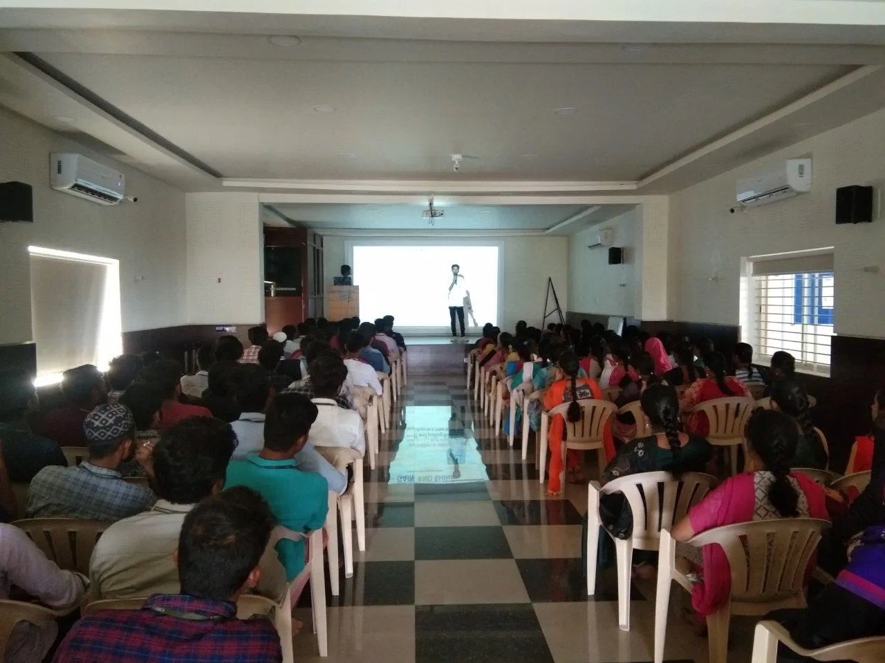 C Sarath Babu's writing on the Gain and Shine launch, 2023. A full college hall watching the pitch